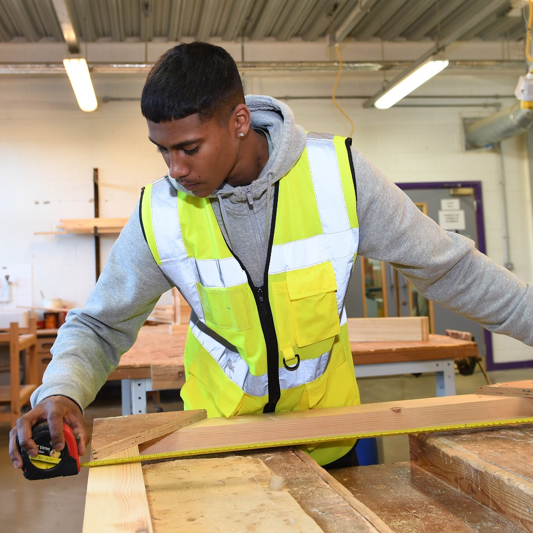 Student in a hi-vis jacket measuring a piece of wood in the carpentry workshop