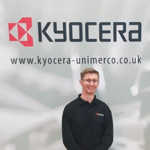 Engineering apprentice Adam Lainchbury standing in front of his company logo - Kyocera