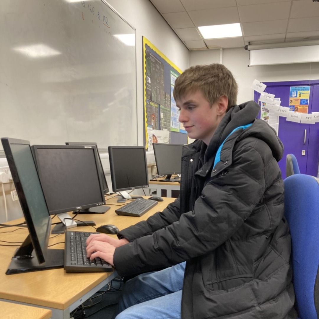 IT student Dominic Rollason-Hough wearing a black coat sitting at a desktop PC