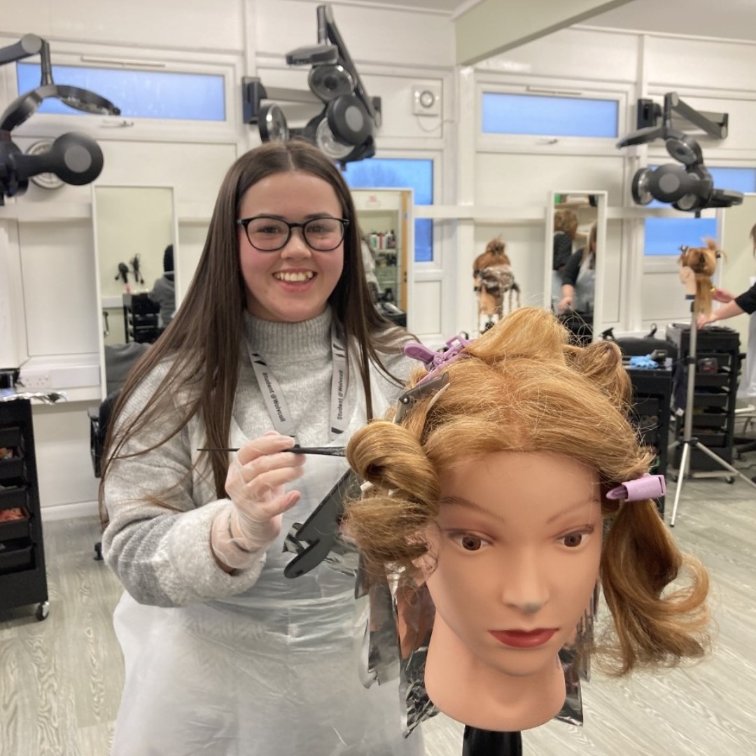 Hairdressing student Jessica Dodd, wearing a grey jumper, practicing a hair cut on a training dummy