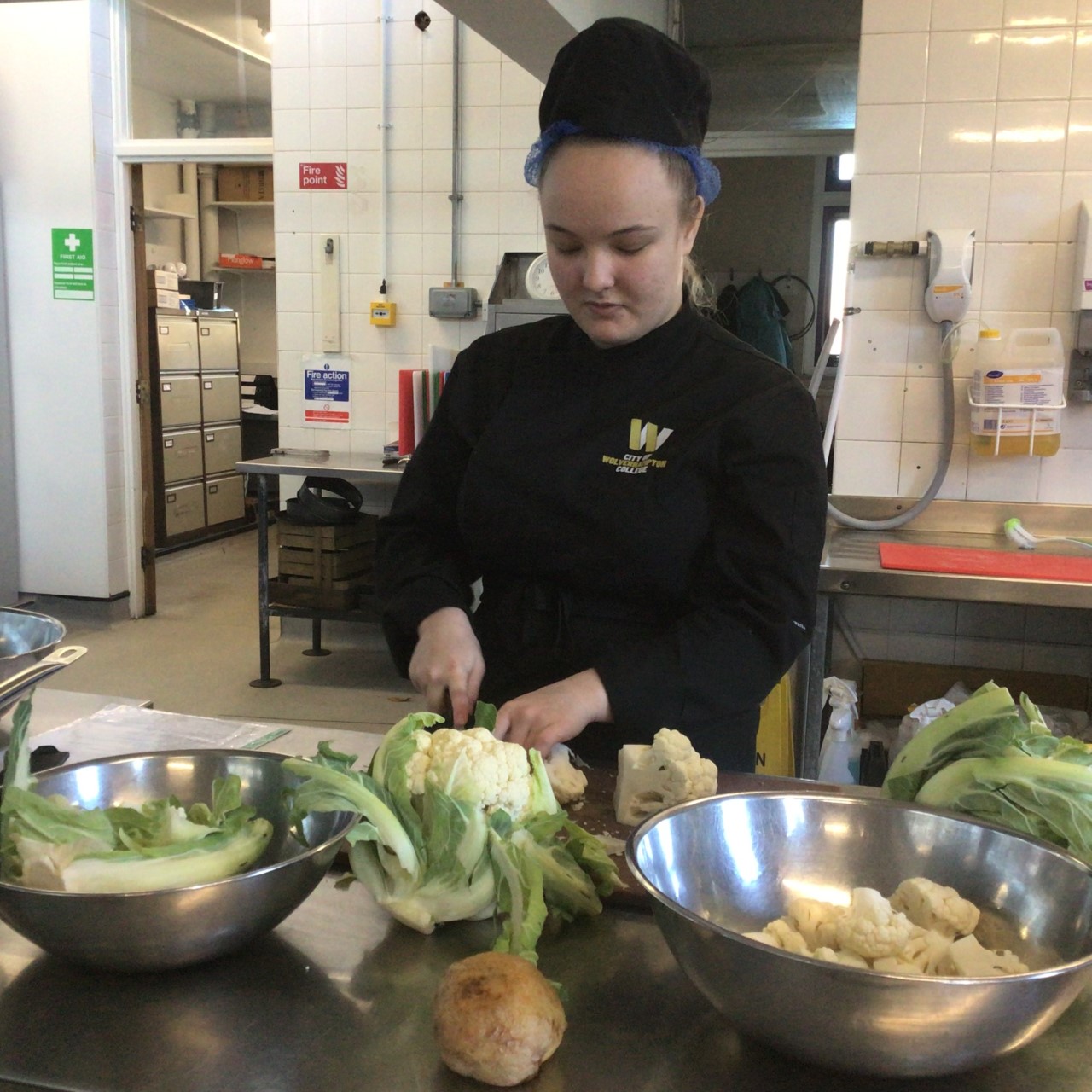 Professional cookery student Mercedes Banks, wearing a black uniform, preparing vegetables in the training kitchen