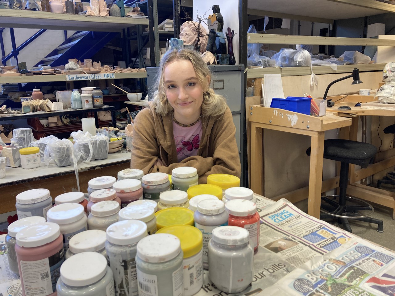 Art student Naomi Hardwick next to pots of paint in the art and design workshop