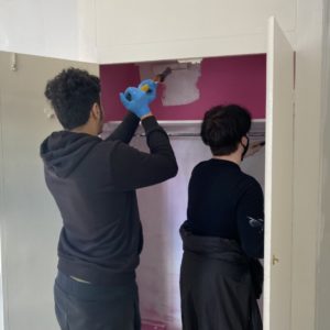 Two students painting the inside of a cupboard with white paint