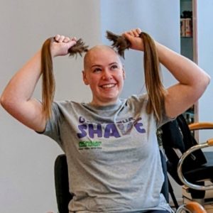 Customer Fay Yates, wearing a grey t-shirt and holding two bumches of long hair after her head was shaved in aid of charity