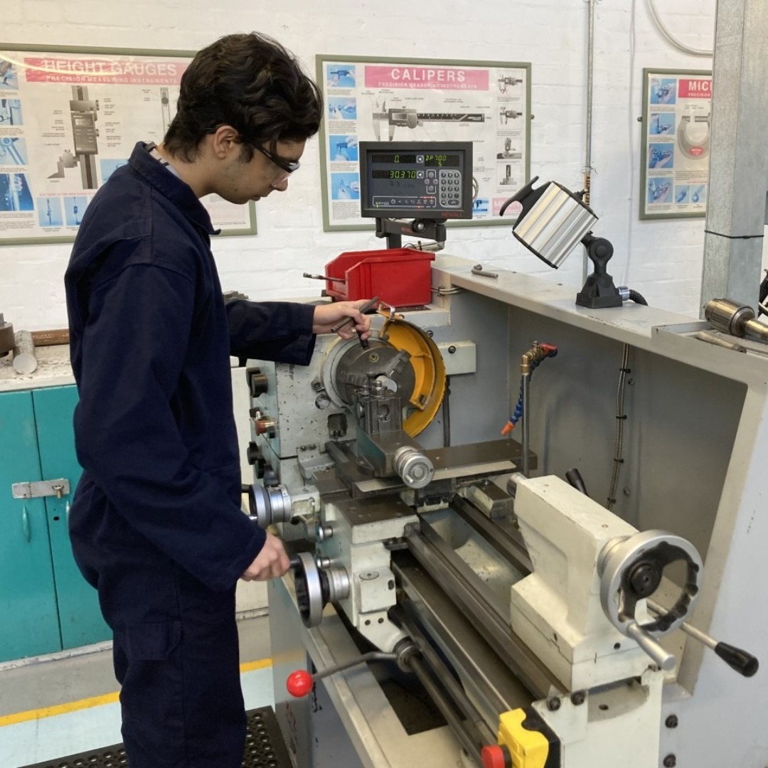Engineering student wearing a dark blue overall working on a piece of equipment in the engineering workshop