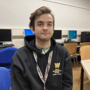 Games design student Adam Cater, wearing a black hoodie embroidered with the college logo, in yellow and white, on the left side