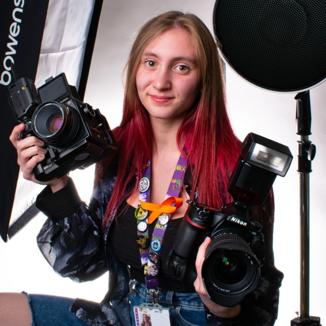 Photography student Rhiannon Cooper posing with two cameras in the college's photography studio