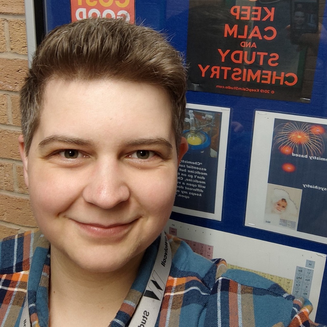 A level student Paulina Patzova wearing a checked shirt and standing in front of a notice board