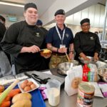 Two cookery students in black uniforms, pictured with a chef from 167 Catering Support Unit