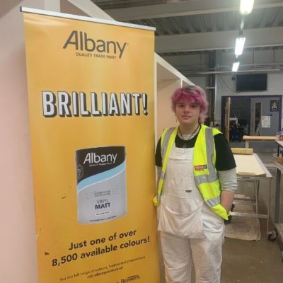 Painting and decorating student Trinity Mason, wearing white overalls and a fluorescent hi-vis jacket