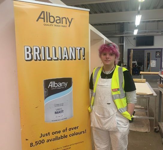Painting and decorating student Trinity Mason, wearing white overalls and a fluorescent hi-vis jacket