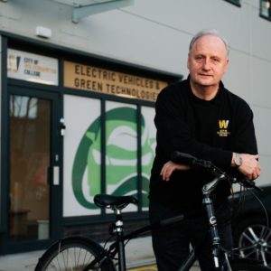 Tutor Paul Mangan wearing a black college sweatshirt, pictured with his bike outside the college's Electric Vehicle training centre