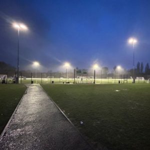 Picture looking across the football pitch at six illuminated floodlights against a dark sky