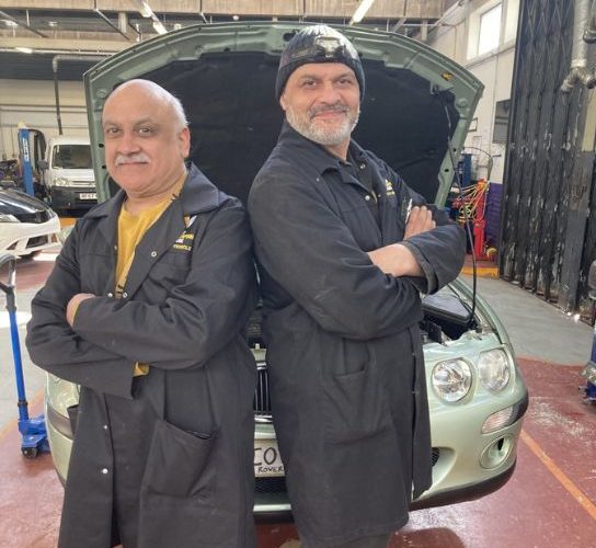 Pete (left) and Kieron Takyar, both wearing blue overalls, in the automotive workshop at the Paget Road campus