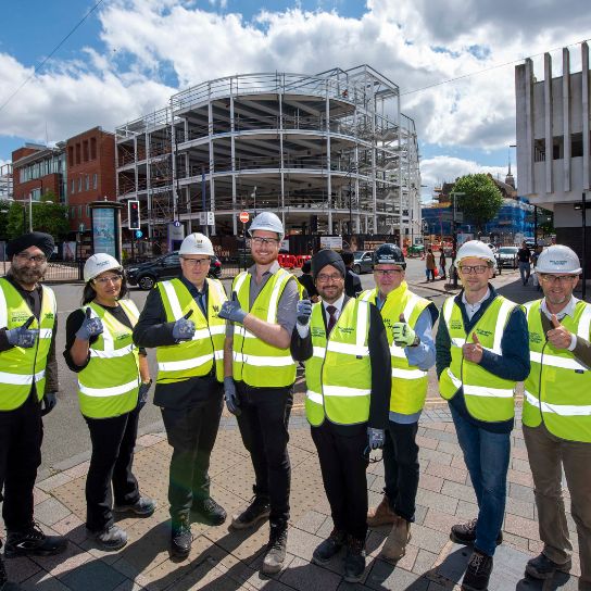 City partners wearing yellow high-vis jackets in front of the steel framework for the new college campus
