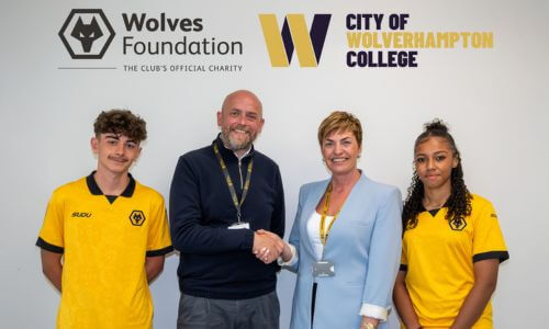 A representative of the college and Wolves Foundation shaking hands on the agreement. They are standing in front of a wall that has both organisation's logos on and are flanked by two Academy players wearing Wolves kit.