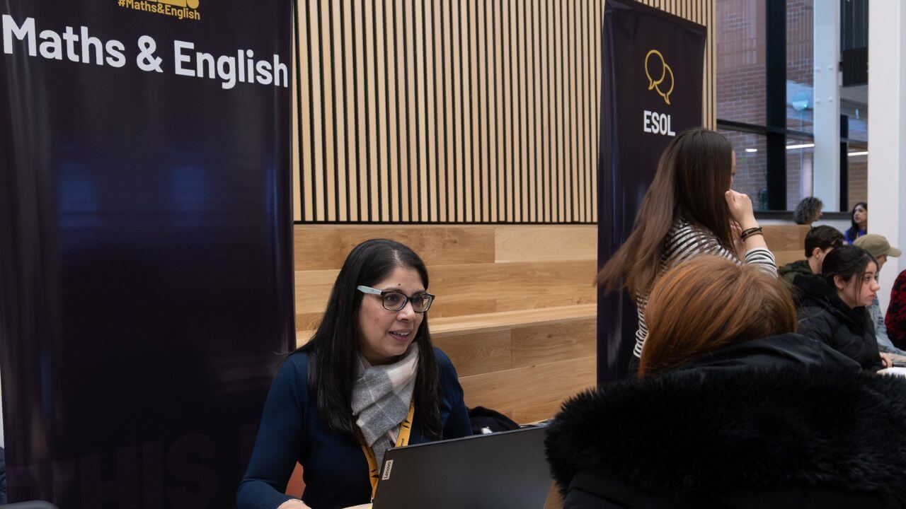 A tutor at a laptop at a desk talking to a prospective student