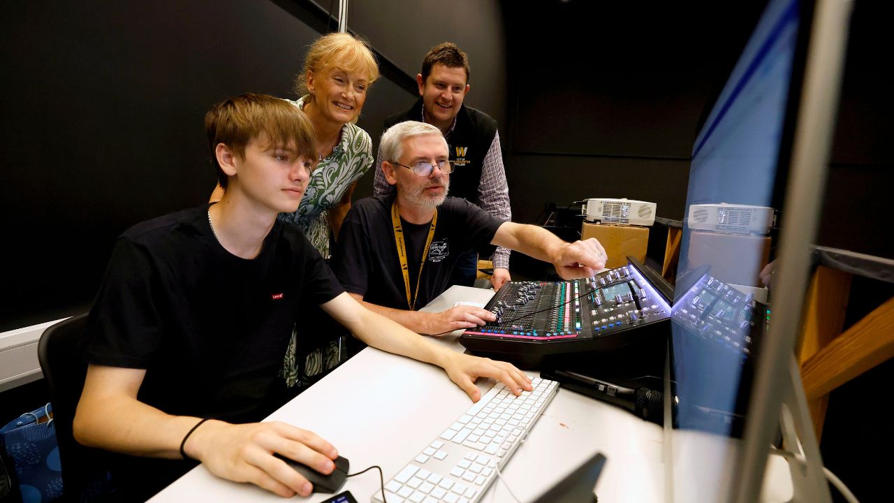 A student and tutor using equipment in the music studio watched by a representative from the college and the theatre.